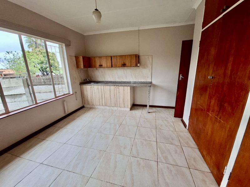 A functional kitchen area featuring built-in cabinetry, stone countertops, a stainless steel sink, and tiled flooring, offering a blank canvas for updates.