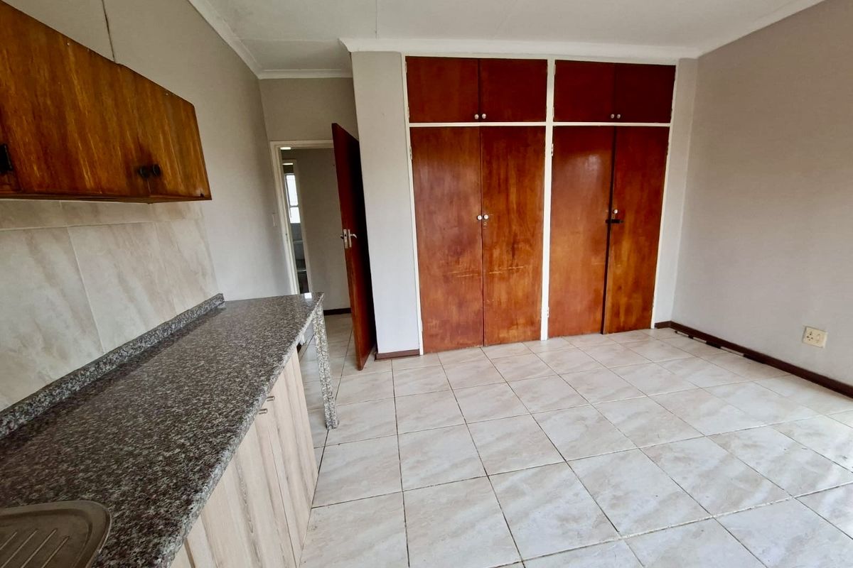 A functional kitchen area featuring tiled flooring, granite countertops, a stainless steel sink, and ample built-in wooden cabinetry for storage.