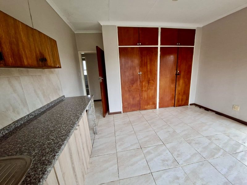 A functional kitchen area featuring tiled flooring, granite countertops, a stainless steel sink, and ample built-in wooden cabinetry for storage.