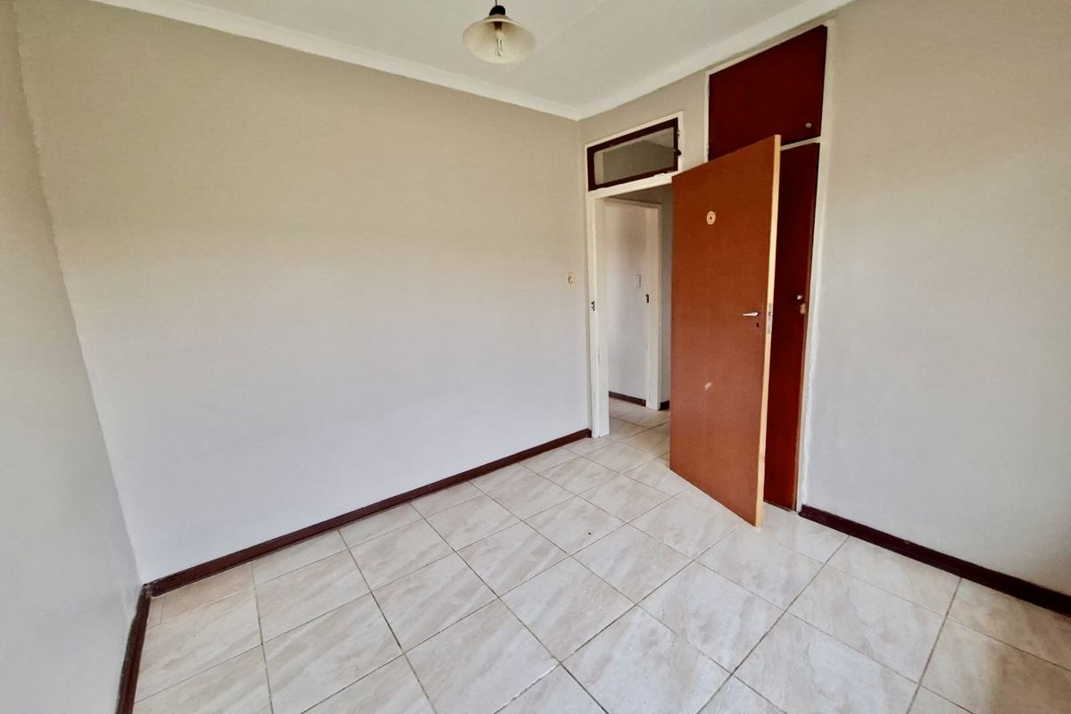 An empty bedroom featuring tiled flooring, a built-in cupboard, and neutral wall finishes, ready for personalization.