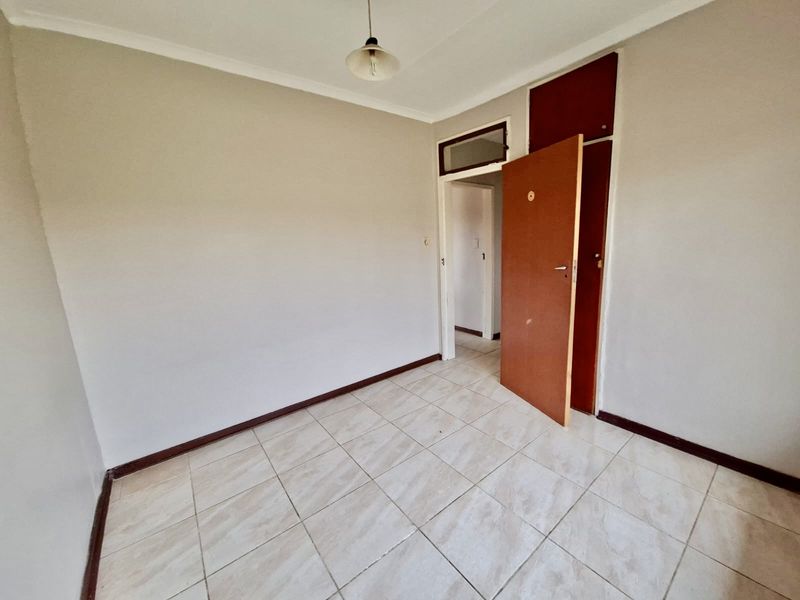 An empty bedroom featuring tiled flooring, a built-in cupboard, and neutral wall finishes, ready for personalization.