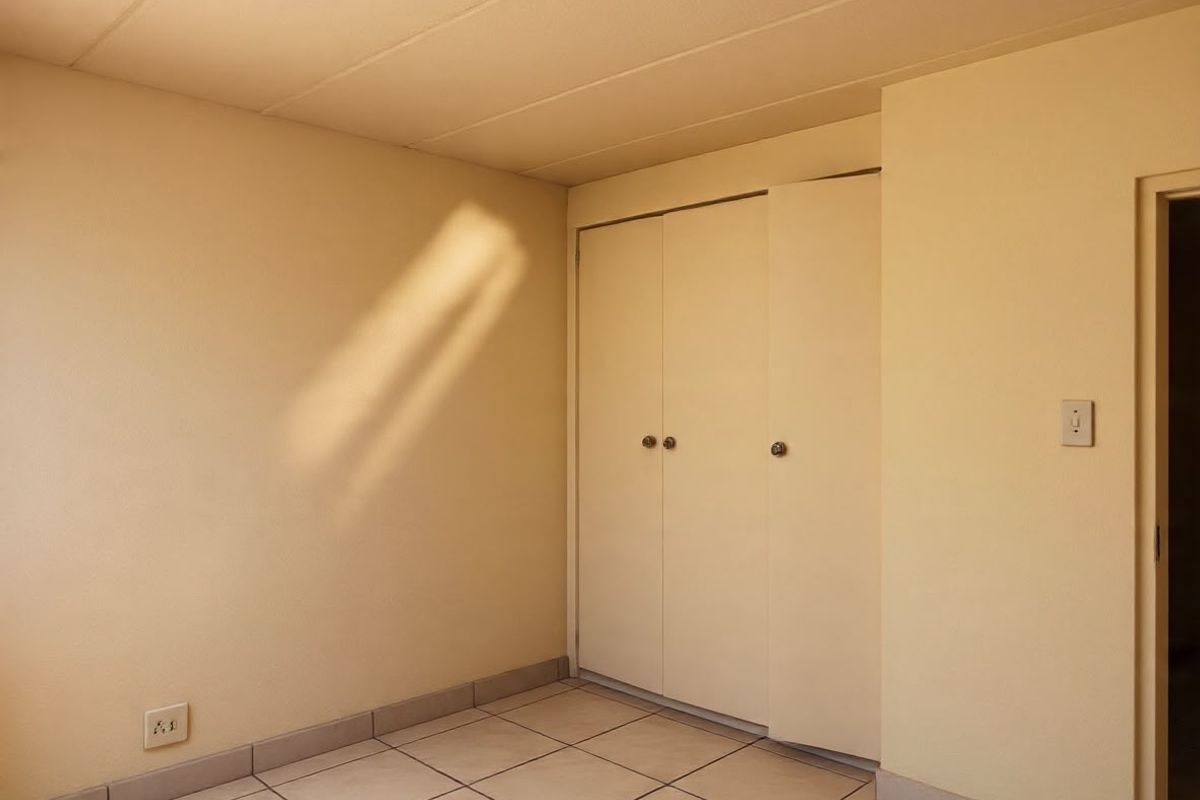 An empty bedroom featuring neutral tiled flooring and a built-in cupboard with sliding doors.