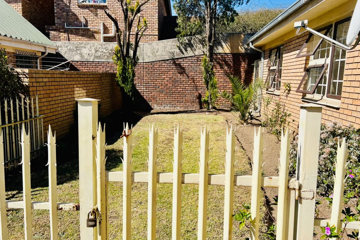 A private rear garden area featuring a lawn, brick boundary walls, and a metal security gate access point.