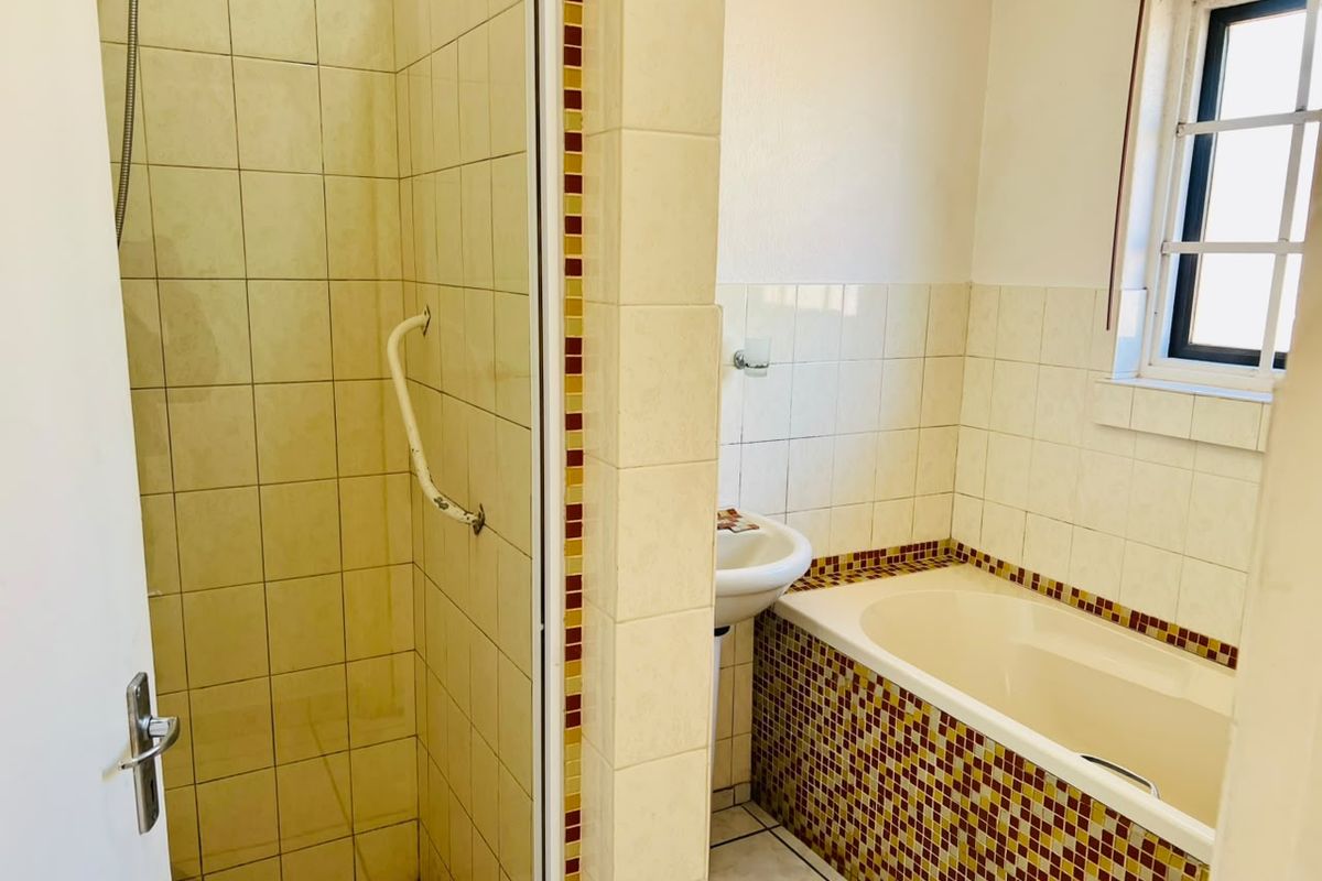 A functional bathroom featuring a shower enclosure with a grab rail, a pedestal basin, and a built-in bathtub with decorative mosaic tile detailing.