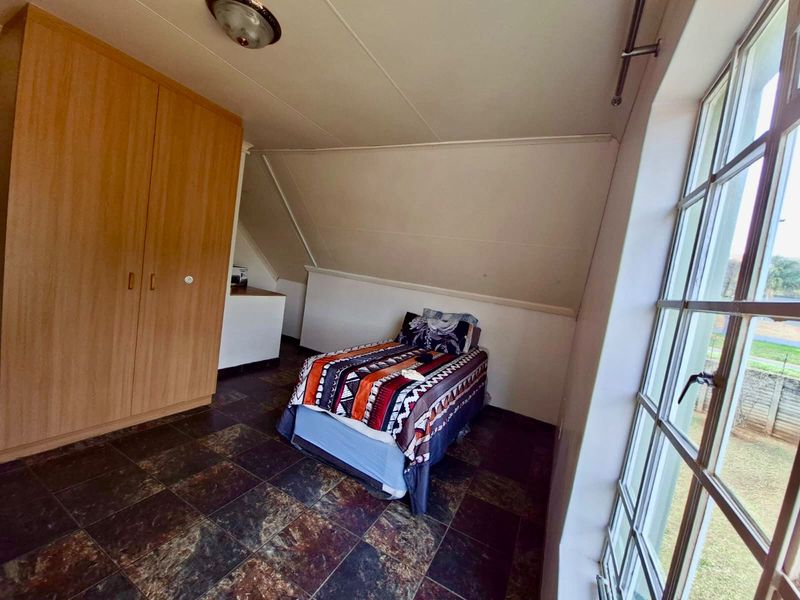 A bedroom featuring tiled flooring, a built-in wardrobe, and a large window with natural light, set under a sloped ceiling.