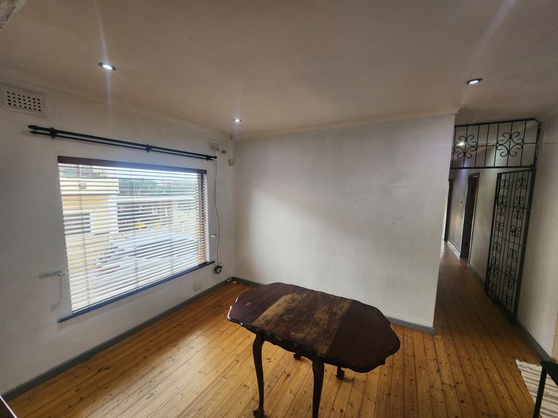 A bright living area featuring polished timber flooring, recessed downlighting, and a security gate leading to the hallway.