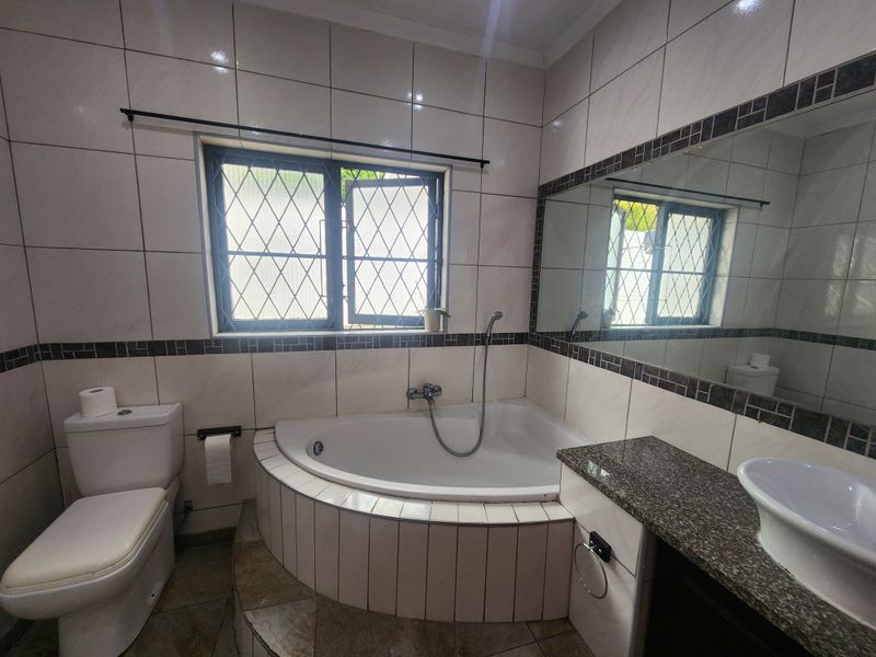 A functional bathroom featuring a corner bathtub, granite-topped vanity with a vessel sink, and tiled finishes throughout.