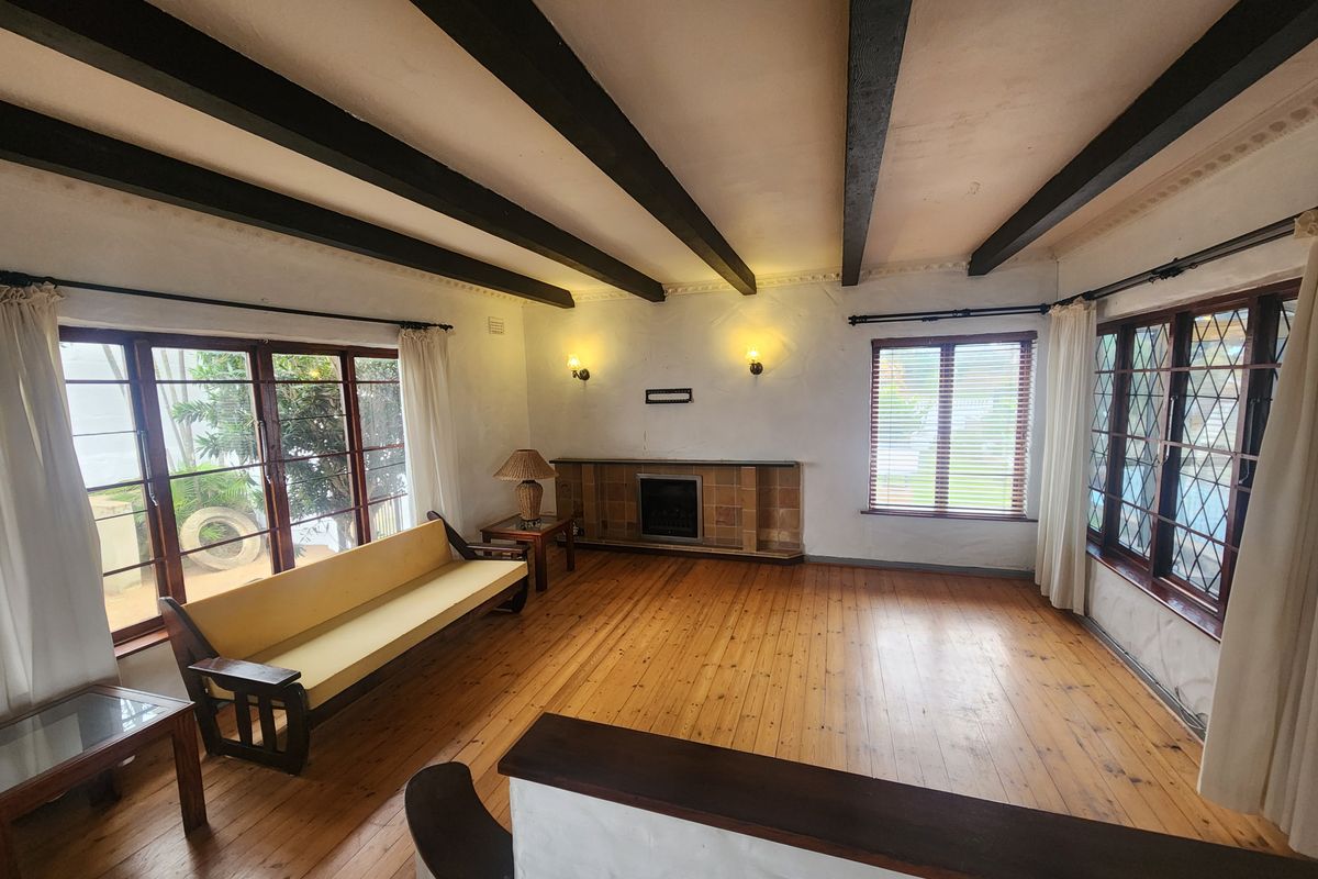 Spacious living room featuring exposed timber ceiling beams, hardwood flooring, and a classic built-in fireplace with a tiled surround.