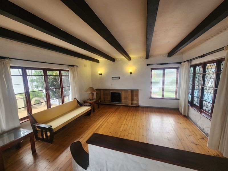 Spacious living room featuring exposed timber ceiling beams, hardwood flooring, and a classic built-in fireplace with a tiled surround.