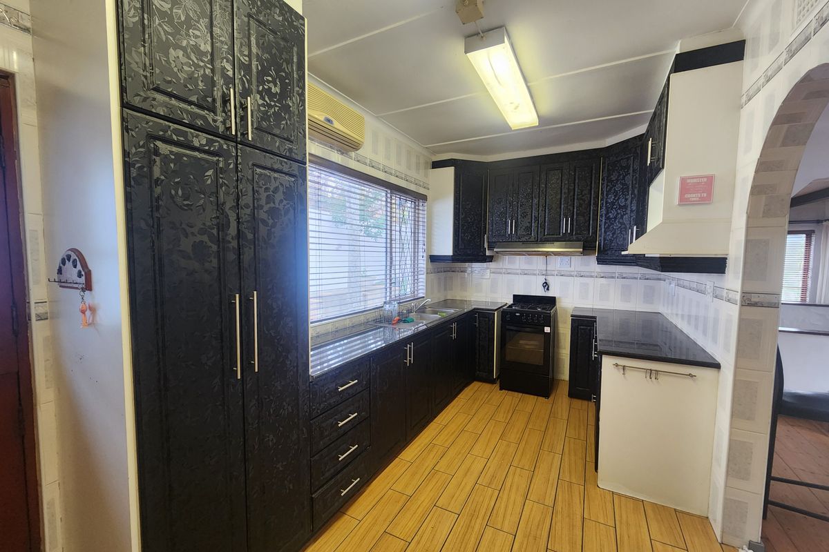 A functional kitchen featuring dark patterned cabinetry, granite countertops, a freestanding stove with extractor fan, and wood-look tiled flooring.