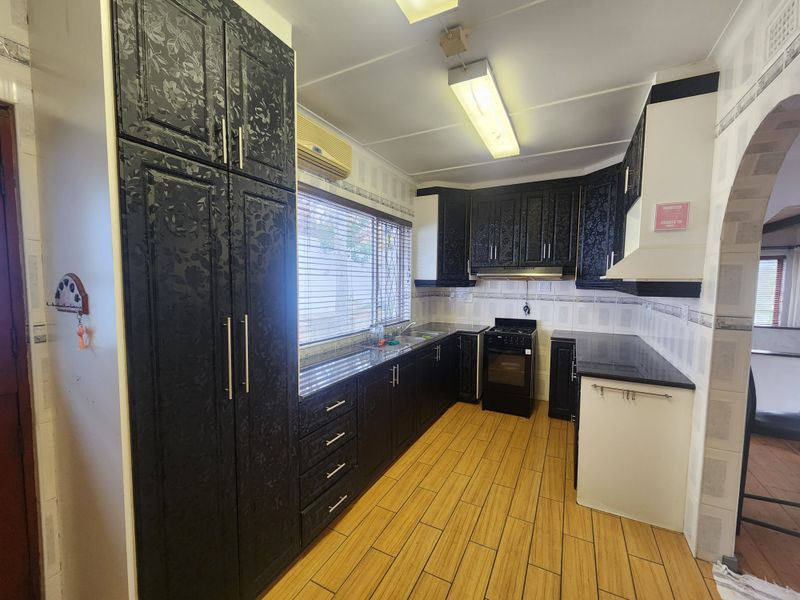 A functional kitchen featuring dark patterned cabinetry, granite countertops, a freestanding stove with extractor fan, and wood-look tiled flooring.