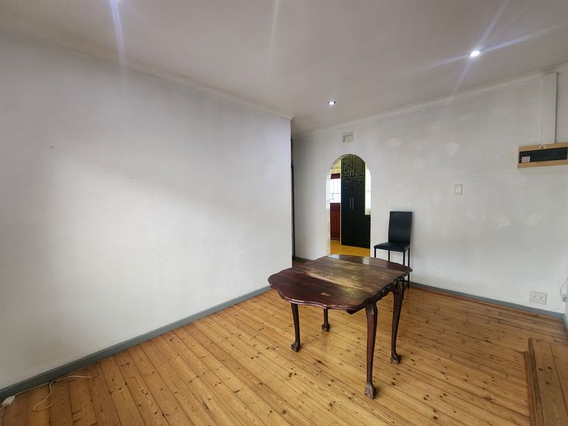 A spacious living area featuring original hardwood flooring, recessed downlighting, and a classic arched doorway leading to the adjacent room.