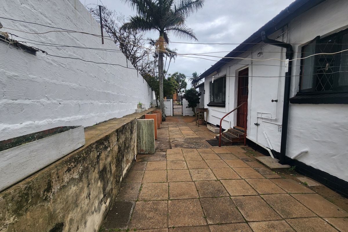 Rear exterior area featuring a paved patio, perimeter wall, and access to the main dwelling, showing signs of weathering and maintenance requirements.