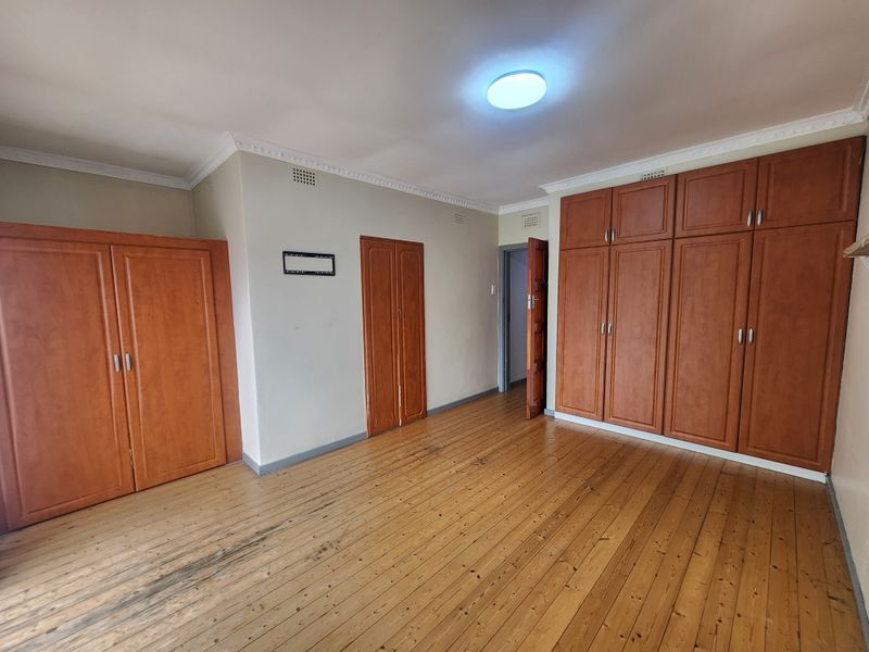 Spacious bedroom featuring original timber flooring, extensive built-in wooden cabinetry, and classic ceiling cornice detailing.
