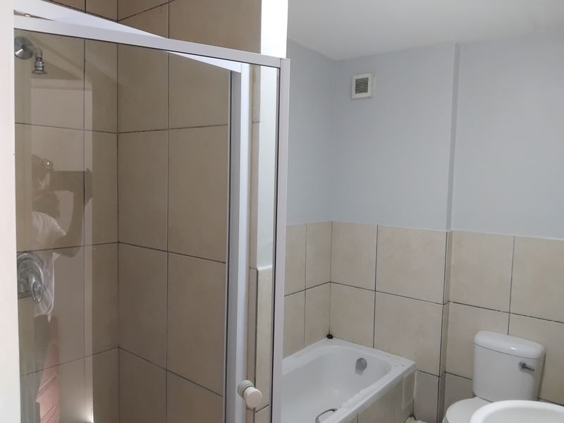 A functional bathroom featuring a shower enclosure, bathtub, toilet, and washbasin with neutral wall tiling.