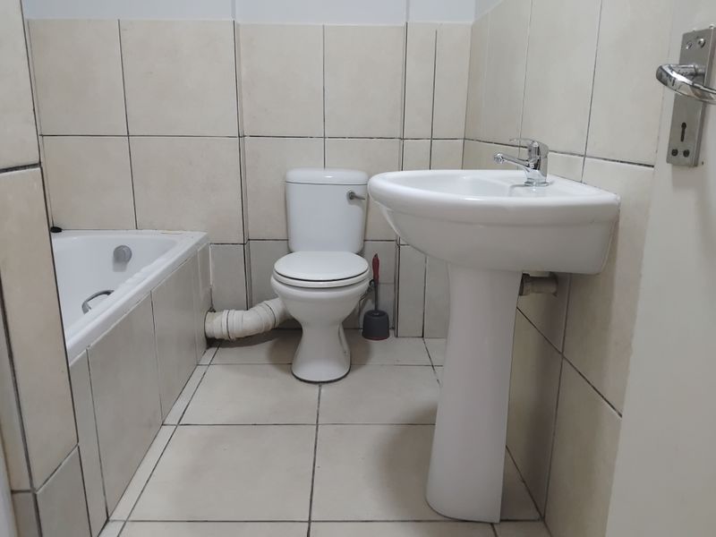A functional bathroom featuring a pedestal basin, toilet, and bathtub with neutral ceramic tiling throughout.