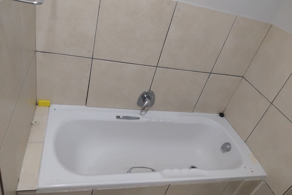 A functional bathroom featuring a built-in bathtub with chrome fixtures and neutral ceramic wall tiling.