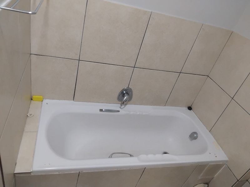 A functional bathroom featuring a built-in bathtub with chrome fixtures and neutral ceramic wall tiling.