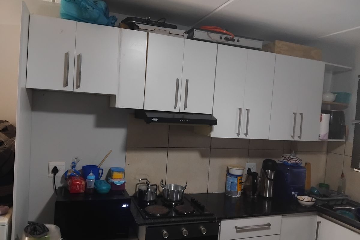 A functional kitchen featuring white built-in cabinetry, a black electric hob, an integrated oven, and a tiled splashback.