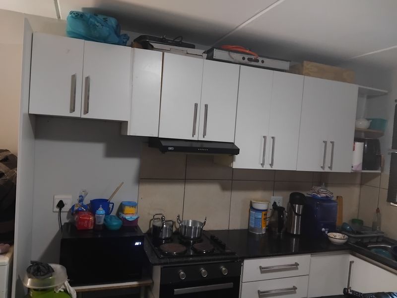 A functional kitchen featuring white built-in cabinetry, a black electric hob, an integrated oven, and a tiled splashback.