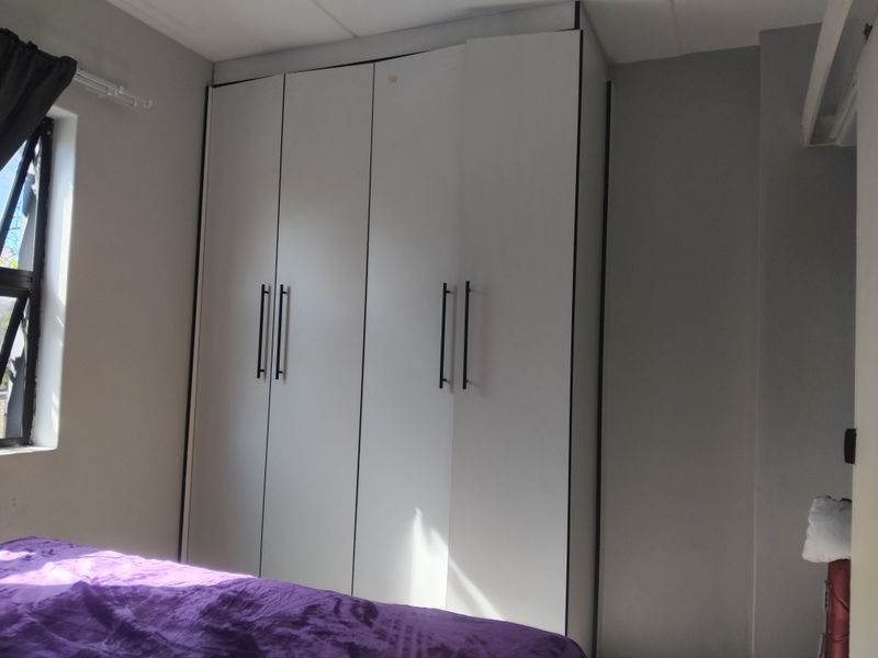 A bedroom featuring a modern white built-in wardrobe with black handles and a side window providing natural light.