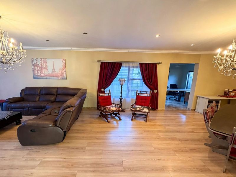 Spacious open-plan living and dining area featuring light laminate flooring, decorative crystal chandeliers, and recessed ceiling lighting.