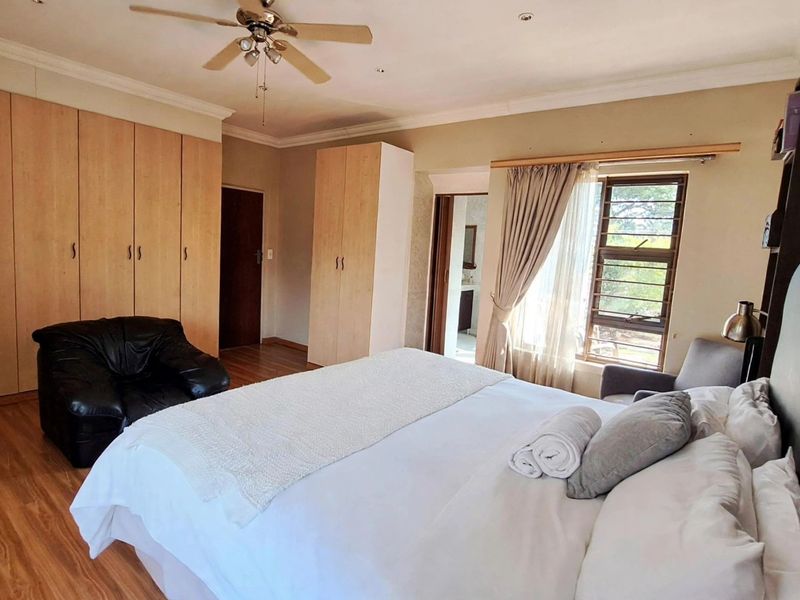 Spacious bedroom featuring extensive built-in cabinetry, laminate flooring, a ceiling fan, and an en-suite bathroom access.