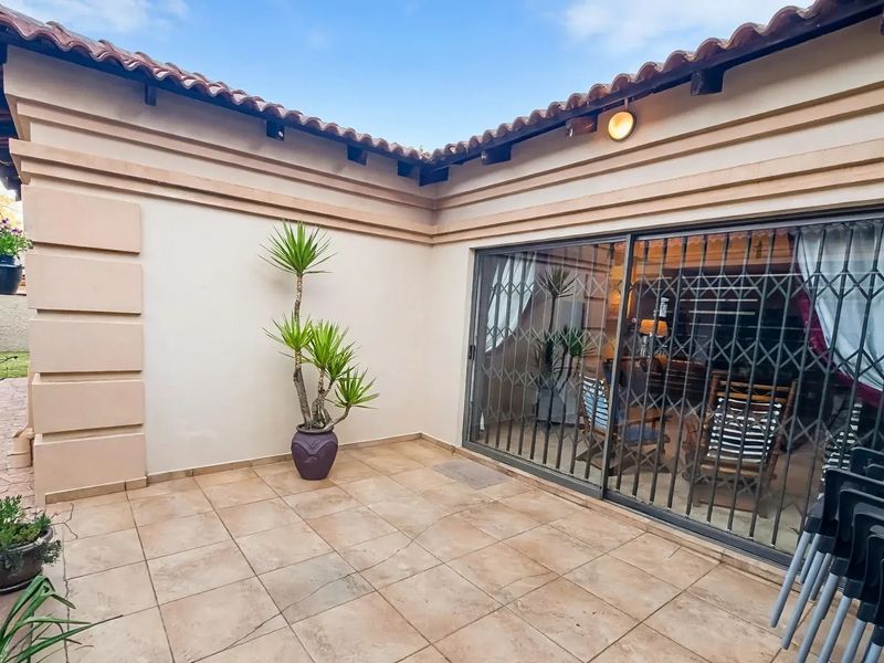 A covered patio area featuring tiled flooring, a sliding glass door with a security gate, and a tiled roof overhang.