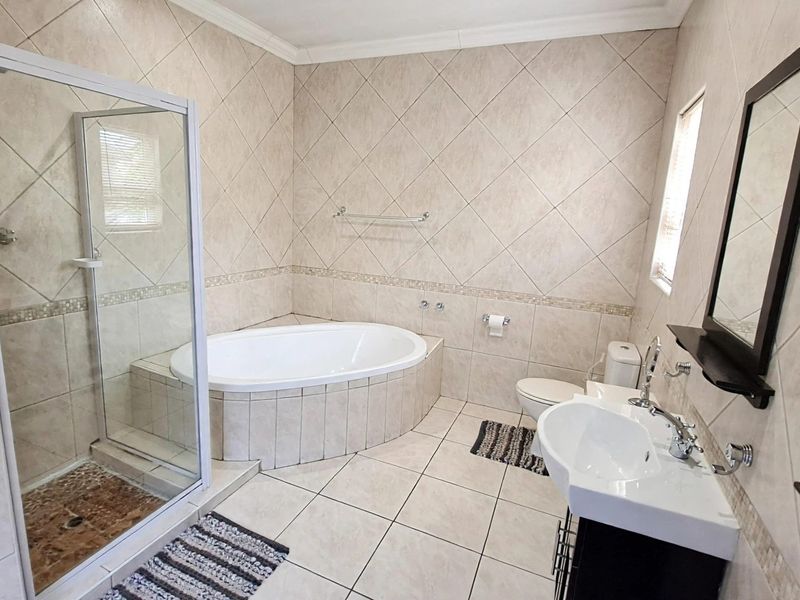 A well-maintained bathroom featuring a built-in bathtub, a separate glass-enclosed shower, a pedestal washbasin, and neutral floor-to-ceiling tiling.