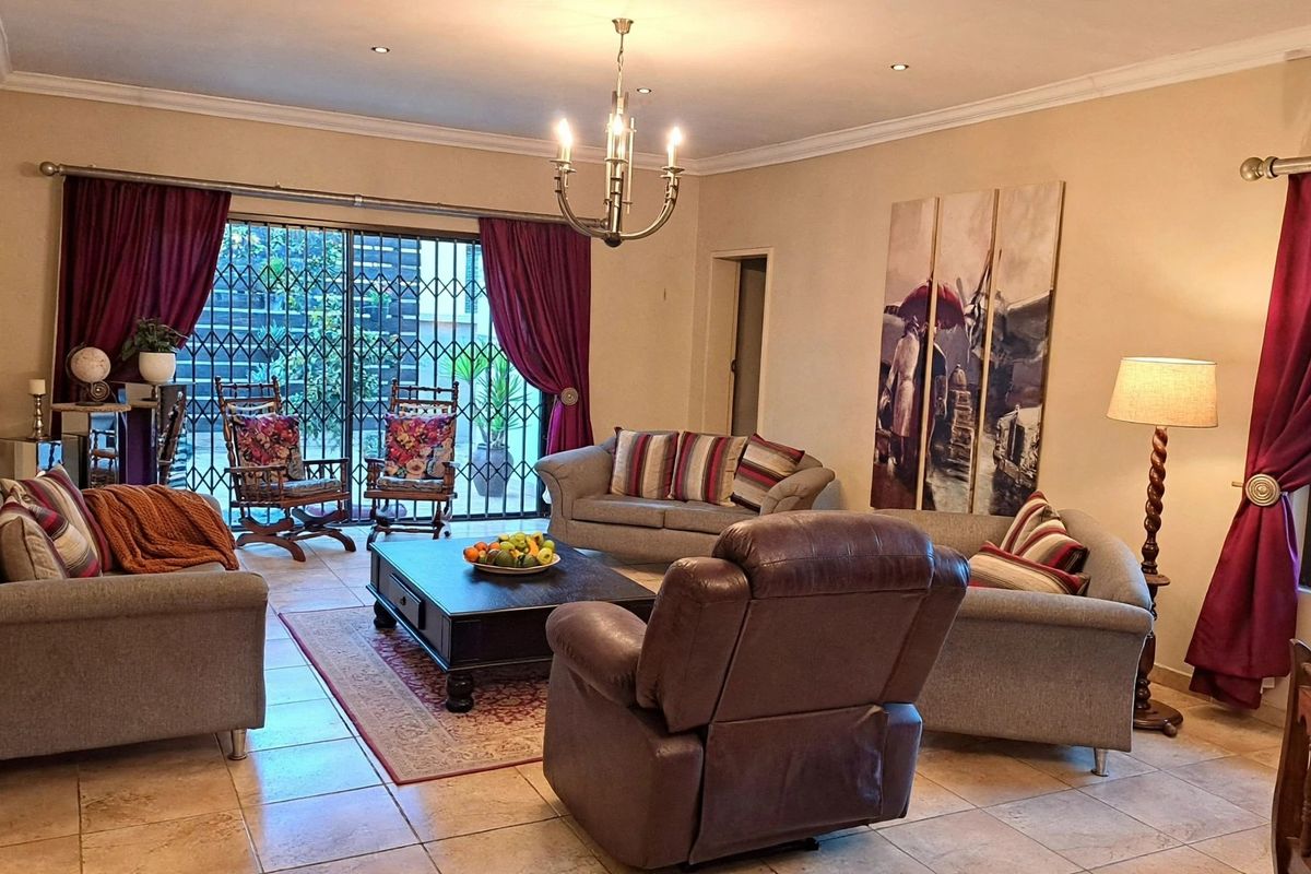 Spacious living room featuring tiled flooring, recessed lighting, a central chandelier, and large sliding glass doors with security gates leading to the exterior.