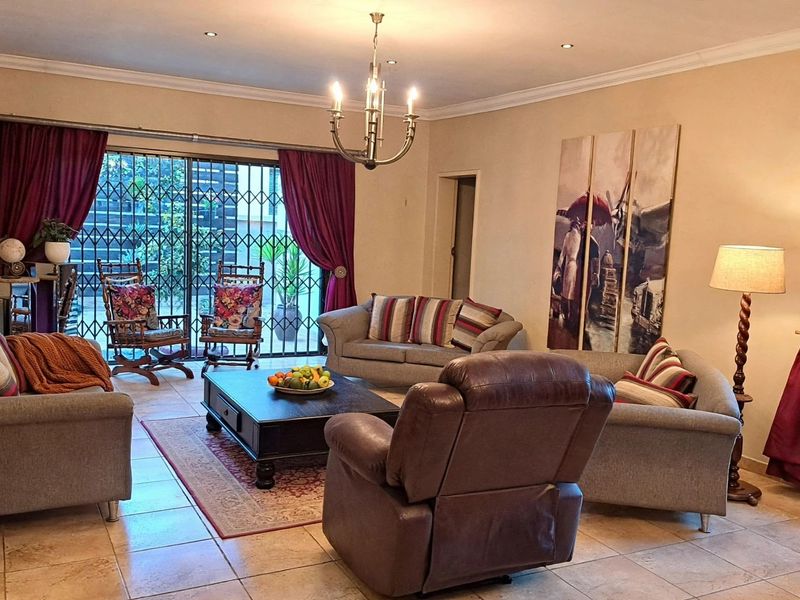 Spacious living room featuring tiled flooring, recessed lighting, a central chandelier, and large sliding glass doors with security gates leading to the exterior.