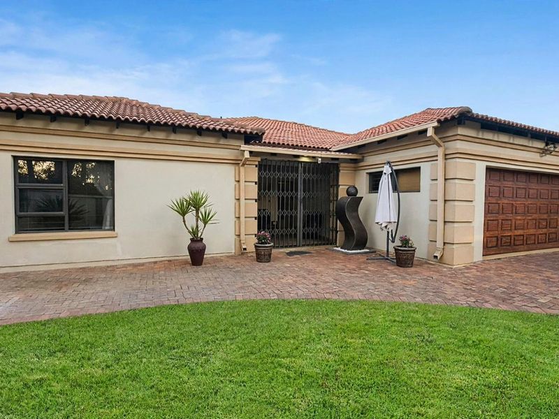 Front elevation of a well-maintained house featuring a paved driveway, tiled roof, integrated garage, and secure entrance gate.