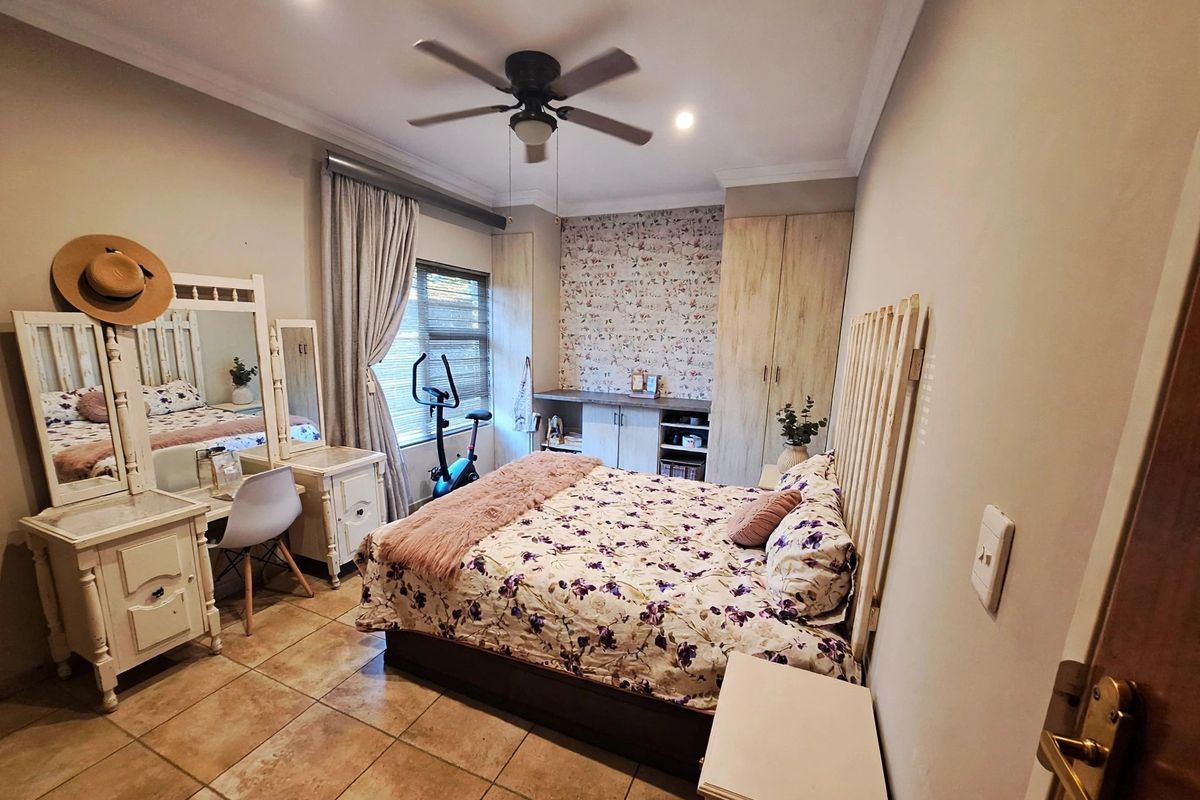 A well-lit bedroom featuring tiled flooring, built-in cupboards, a ceiling fan, and decorative wallpaper accent wall.