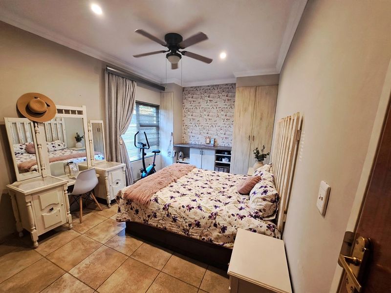 A well-lit bedroom featuring tiled flooring, built-in cupboards, a ceiling fan, and decorative wallpaper accent wall.