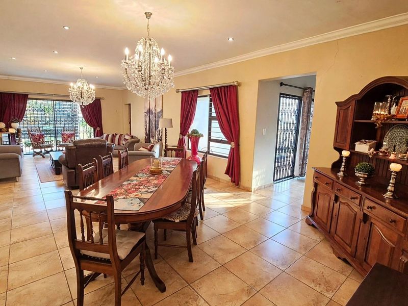 Spacious open-plan living and dining area featuring tiled flooring, elegant crystal chandeliers, and direct access to the outdoor patio through sliding security doors.