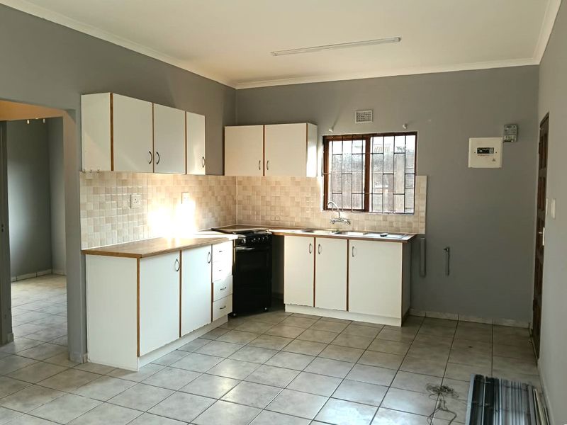A functional kitchen featuring white cabinetry, tiled backsplash, stainless steel sink, and a freestanding stove, with ceramic floor tiles throughout.