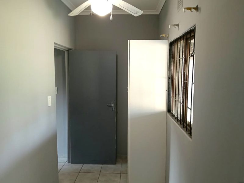 A functional hallway featuring tiled flooring, a ceiling fan, and a window fitted with security bars.