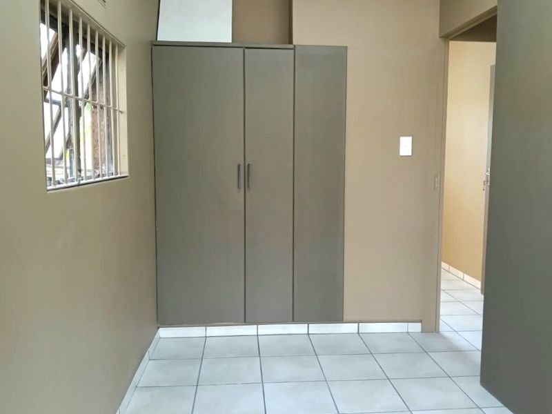 A clean, empty bedroom featuring neutral wall paint, tiled flooring, and a built-in wardrobe with security bars on the window.