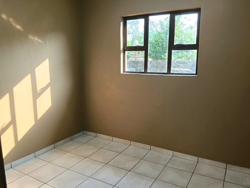 A clean, empty bedroom featuring neutral wall paint, tiled flooring, and an aluminium-framed window providing natural light.