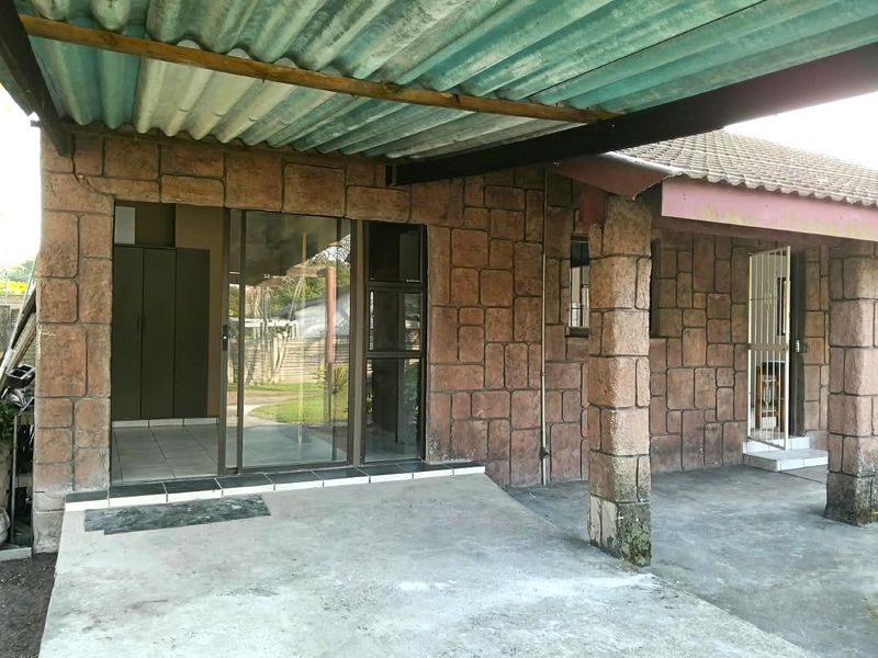 A covered outdoor patio area featuring stone-clad walls, concrete flooring, and a corrugated roof, providing a functional space for outdoor living.