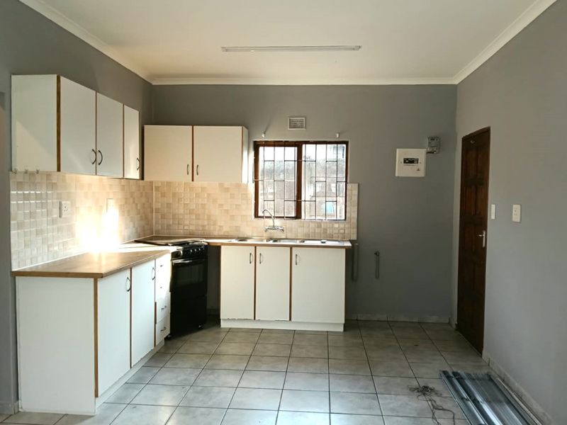 A functional kitchen featuring white cabinetry, tiled backsplash, stainless steel sink, and a freestanding stove, with neutral grey walls and tiled flooring.