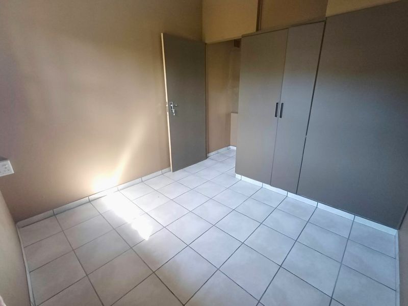 A clean, empty bedroom featuring neutral wall tones, tiled flooring, and built-in cupboards, offering a versatile space ready for personalization.