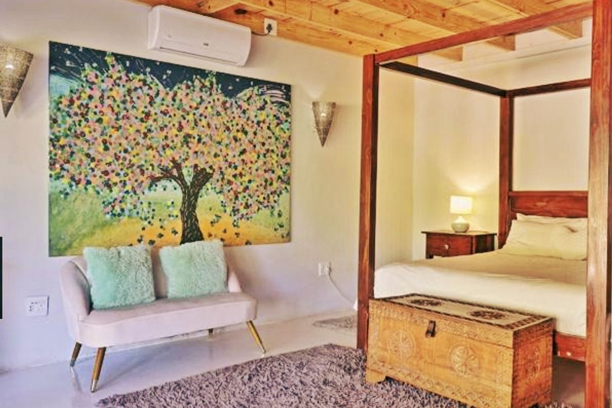 A well-maintained bedroom featuring exposed timber ceiling beams, wall-mounted air conditioning, and decorative wall sconces.