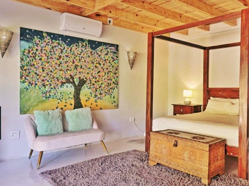 A well-maintained bedroom featuring exposed timber ceiling beams, wall-mounted air conditioning, and decorative wall sconces.