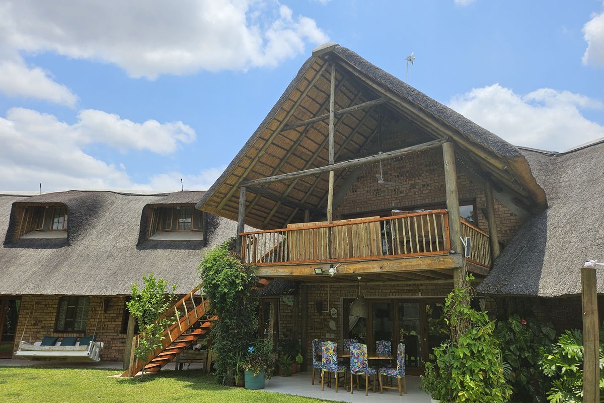 Rear view of a double-story thatched roof house featuring exposed brickwork, a timber balcony, and a covered patio area overlooking the garden.