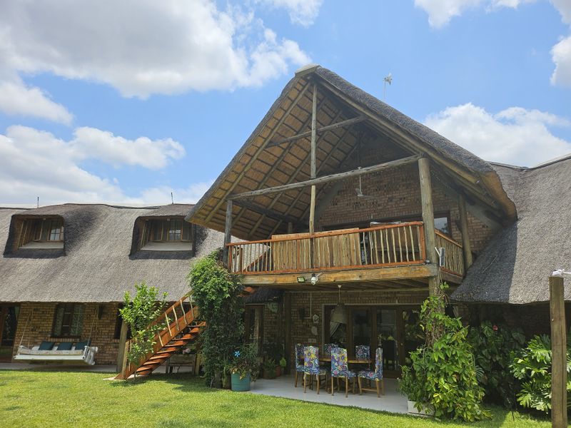 Rear view of a double-story thatched roof house featuring exposed brickwork, a timber balcony, and a covered patio area overlooking the garden.