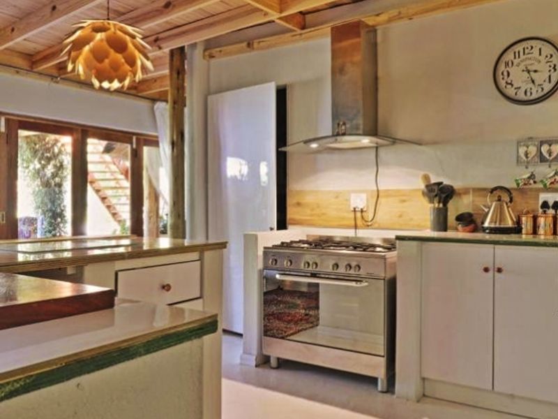 A rustic kitchen featuring exposed timber beam ceilings, stainless steel gas stove with extractor fan, and wooden countertops with direct access to the outdoors.