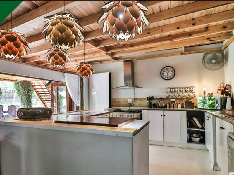 A rustic-style kitchen featuring exposed timber ceiling beams, a central island, and direct access to an outdoor area through large sliding glass doors.