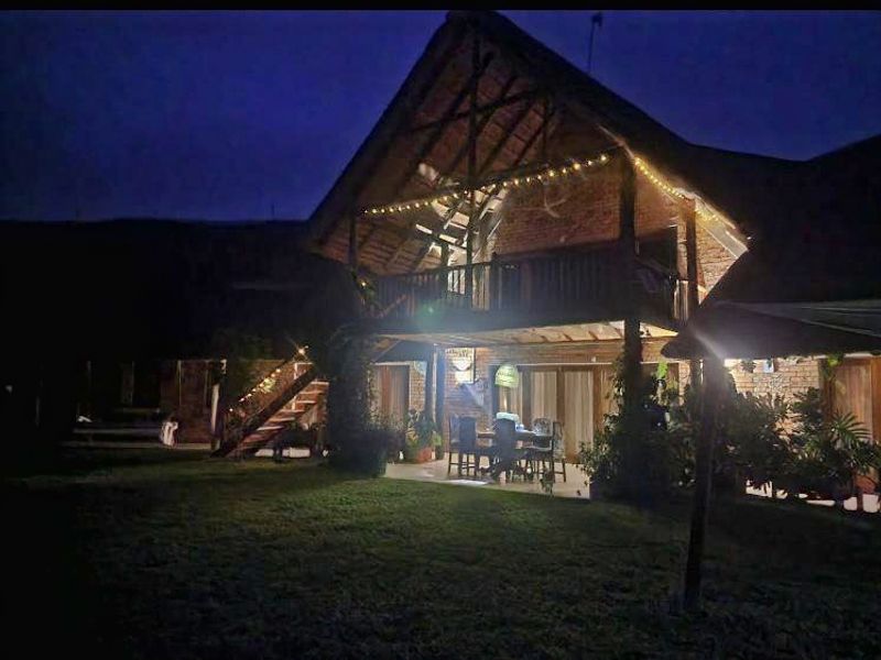 A charming double-story home with a thatched roof, exposed brick facade, and a spacious covered patio overlooking the rear garden at dusk.
