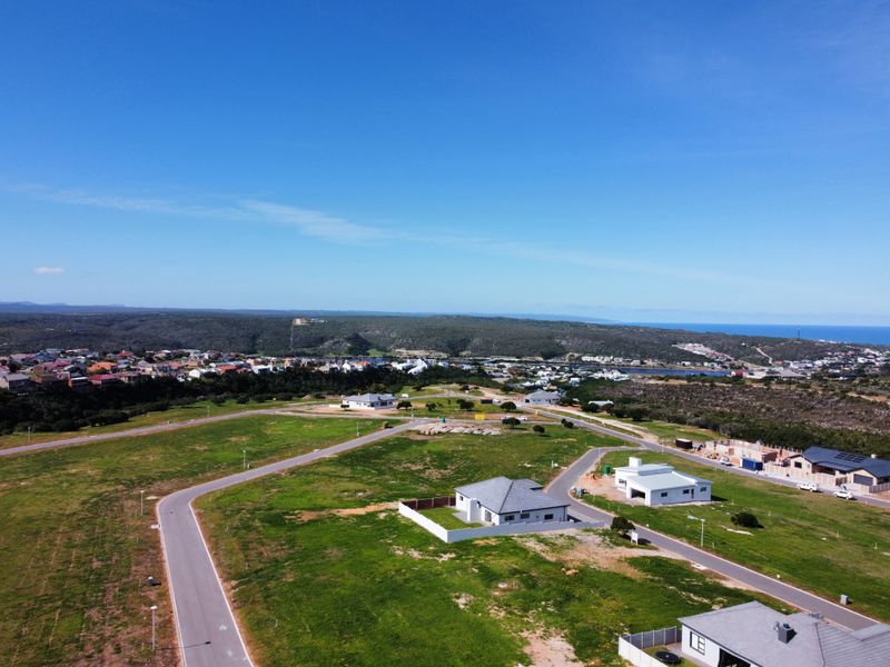 An aerial view of a residential development area featuring paved roads, established plots, and surrounding coastal landscape.
